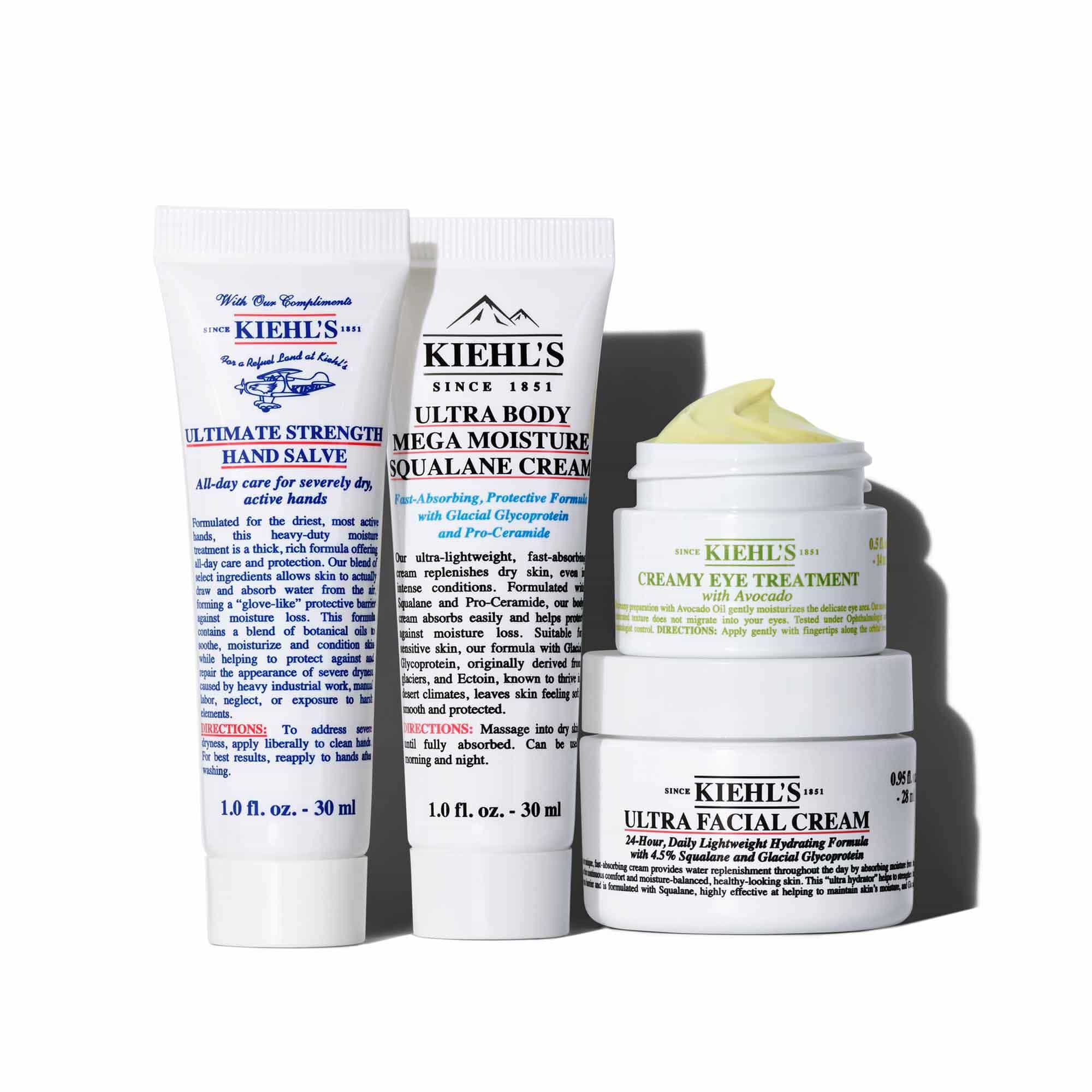 Grafika zobrazujici čtyři bile produkty peče o pleť Kiehl's uspořadane na bilem pozadi. Zleva doprava: tuba "KIEHL'S ULTIMATE STRENGTH HAND SALVE", tuba "KIEHL'S ULTRA BODY MEGA MOISTURE SQUALANE CREAM", mala sklenice "KIEHL'S CREAMY EYE TREATMENT WITH AVOCADO" s viditelnym světle žlutym kremem a větši sklenice "KIEHL'S ULTRA FACIAL CREAM". Sklenice s očnim kremem a kremem na obličej jsou naskladane.