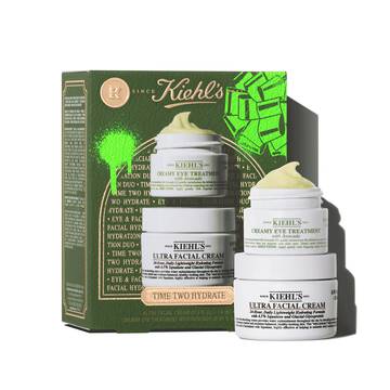 Vlevo je zobrazena zelena darkova krabička Kiehl's s textem "TIME TWO HYDRATE" a zelenymi grafickymi prvky. Vpravo jsou na sobě naskladany dvě sklenice s produkty: horni nadoba je "KIEHL'S CREAMY EYE TREATMENT with avocado" a nahoře ma viditelny žlutozeleny vir produktu. Spodni nadoba je "KIEHL'S ULTRA FACIAL CREAM".