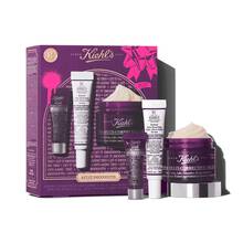 Grafika znazorňujici fialovou darkovou krabičku Kiehl's se zlatymi akcenty vlevo. Krabice obsahuje tři produkty. Napravo od krabice jsou mimo krabici zobrazeny stejne tři produkty: mala fialova tuba "Kiehl's Super Multi-Corrective Eye Zone Treatment", bila a fialova tuba "Kiehl's Retinol Skin-Renewing Daily Micro-Dose Serum" a fialova nadoba "Kiehl's Super Multi-Corrective Cream" s viditelnym kremem. Krabička je zdobena jasně růžovymi grafickymi střikanci barvy a vzorem mašle a ve spodni časti ma text "LET IT SMOOOOOTH".