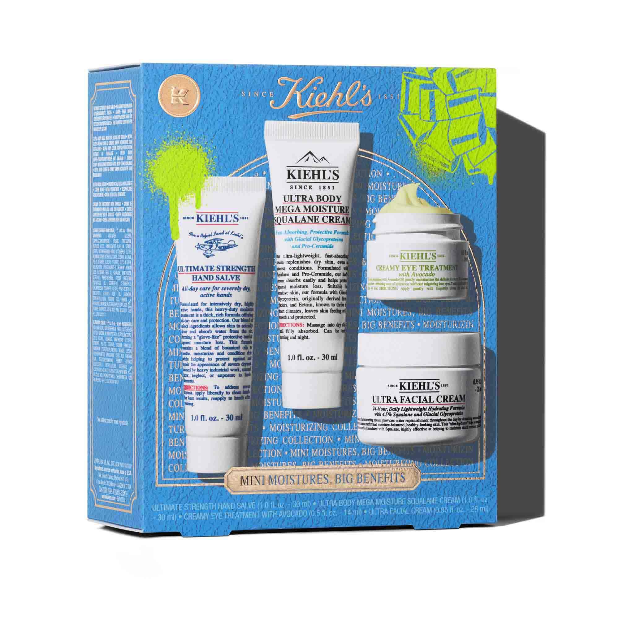 Grafika s modrou darkovou krabičkou Kiehl's se zelenymi akcenty. Krabička obsahuje čtyři produkty: tubu "KIEHL'S ULTIMATE STRENGTH HAND SALVE", tubu "KIEHL'S ULTRA BODY MEGA MOISTURE SQUALANE CREAM", sklenici "KIEHL'S CREAMY EYE TREATMENT WITH AVOCADO" a sklenici "KIEHL'S ULTRA FACIAL CREAM". Krabička je zdobena jasně zelenymi grafickymi střikanci barvy a designem mašle a ve spodni časti ma text "MINI MOISTURES, BIG BENEFITS".