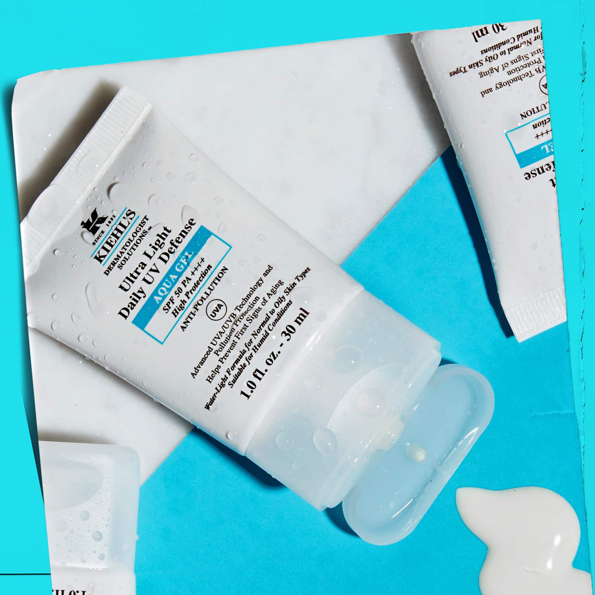 Ploche uspořadani vice tub Ultra Light Daily UV Defense Aqua Gel na mramorovem povrchu, ukazujici jejich lifestylovy vzhled.