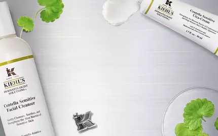 Obrazek produktu Kiehl's s čisticim prostředkem na obličej, umistěnym na střibrnem pozadi s dekorativnimi prvky, jako jsou rostliny a laboratorni sklo.