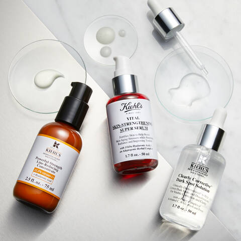 Tři kosmeticke produkty Kiehl's na mramorove desce: serum s posilujicimi latkami, revitalizačni serum a serum na tmave skvrny.