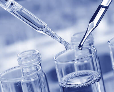 Two pipettes are shown above a glass container filled with liquid, with one pipette poised to release a drop. The image has a blue-tinted color scheme.