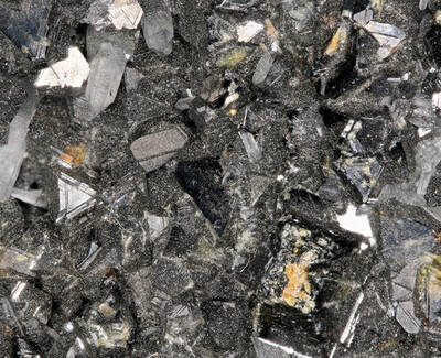 A close-up of shiny, crystal-like minerals with a dark, textured background, showcasing various shapes and reflections.