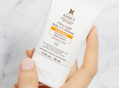 Ruka drži krem na opalovani Kiehl's Ultra Light Daily UV Defense, 30 ml, s ochranou před UVA a UVB paprsky.