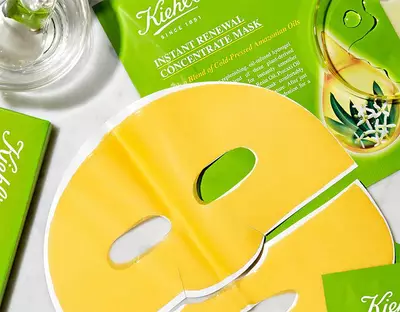 Žluta pleťova maska Kiehl's na bilem pozadi s prazdnou krabičkou a skleněnou lahvičkou.