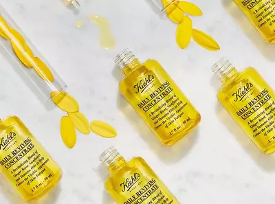 Sada lahviček s olejem Kiehl's Daily Reviving Concentrate na mramorovem pozadi s okvětnimi listky.