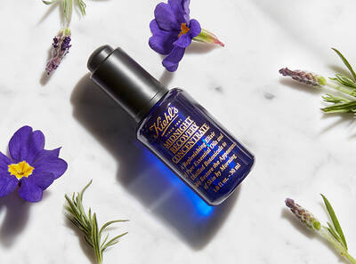 Modra lahvička s hydratačnim olejem na pleť s levanduli a fialkami na mramorove ploše.