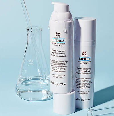 Bile serum Kiehl's Hydro-Plumping s laboratornimi nastroji na modrem pozadi.