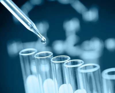 A pipette is about to drop a liquid into a row of clear test tubes, with a blurred DNA sequence graphic in the background.