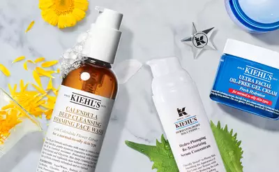 Image of Kiehl's skincare products on a marble surface. Featured items include a foaming face wash, a hydrating serum concentrate, and an oil-free gel cream, accompanied by yellow flower petals and green leaves for a natural aesthetic.