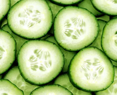 A close-up view of several cucumber slices arranged closely together, showcasing their vibrant green skin and light green flesh with visible seeds.