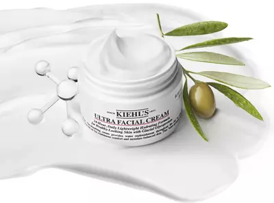 Krem Kiehl's Ultra Facial Cream obklopeny olivovymi větvičkami a bilou kremovou texturou na pozadi.